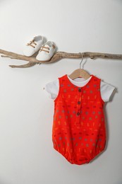 Baby bodysuit and booties on decorative branch near light grey wall
