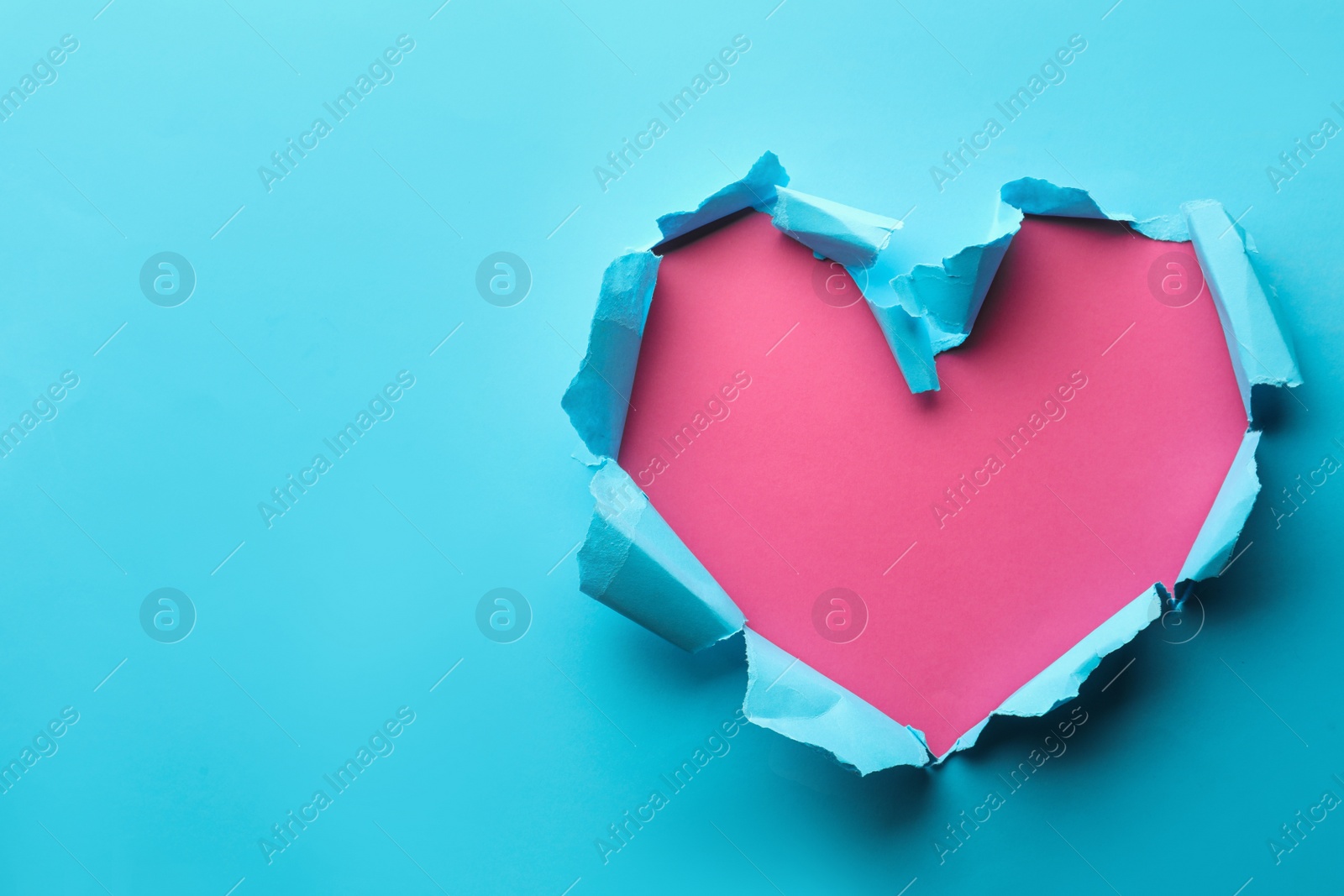 Photo of Torn heart shaped hole in light blue paper on pink background, space for text