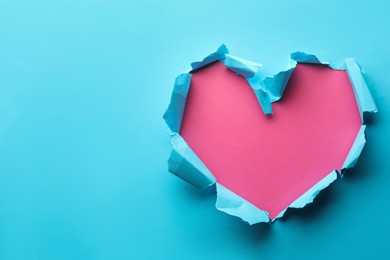 Photo of Torn heart shaped hole in light blue paper on pink background, space for text