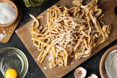 Board with homemade pasta, flour and ingredients on dark table, flat lay