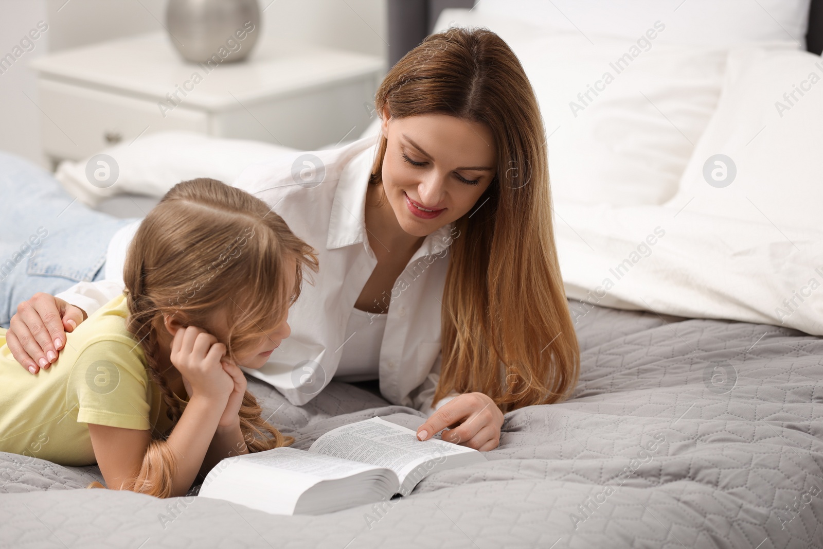 Photo of Girl and her godparent reading Bible together on bed at home