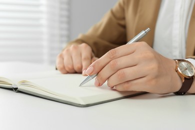 Photo of Woman writing in notebook at white table, closeup