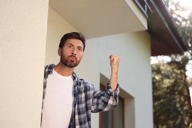 Photo of Angry man showing fist near house, low angle view. Annoying neighbour