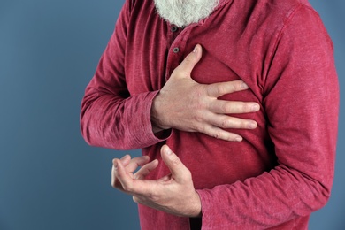 Mature man having heart attack on color background