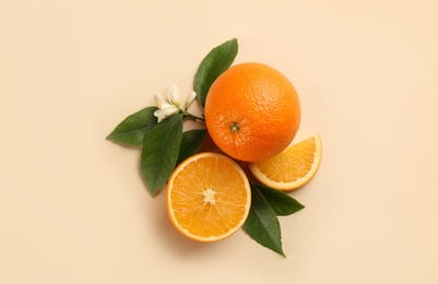 Photo of Fresh ripe oranges with green leaves and flower on beige background, flat lay