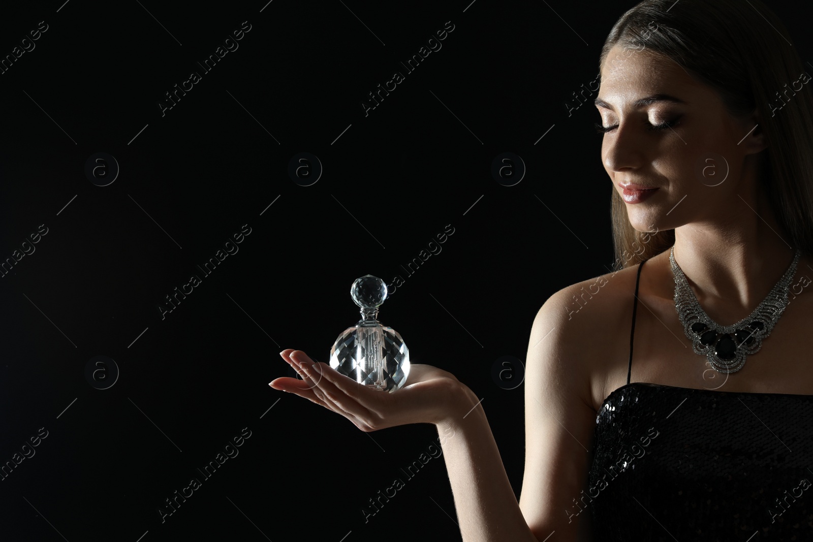 Photo of Young woman with bottle of perfume on black background. Space for text