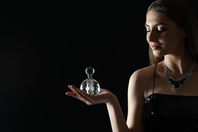 Young woman with bottle of perfume on black background. Space for text