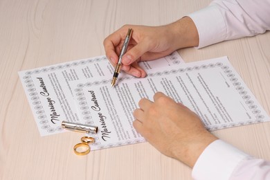 Man signing marriage contract at light wooden table, closeup