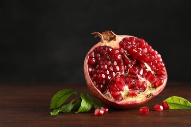 Photo of Cut fresh pomegranate and green leaves on wooden table, closeup. Space for text