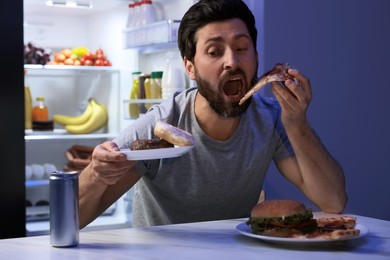 Photo of Man eating junk food in kitchen at night. Bad habit