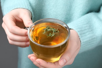 Photo of Woman holding cup of tasty herbal tea with thyme, closeup