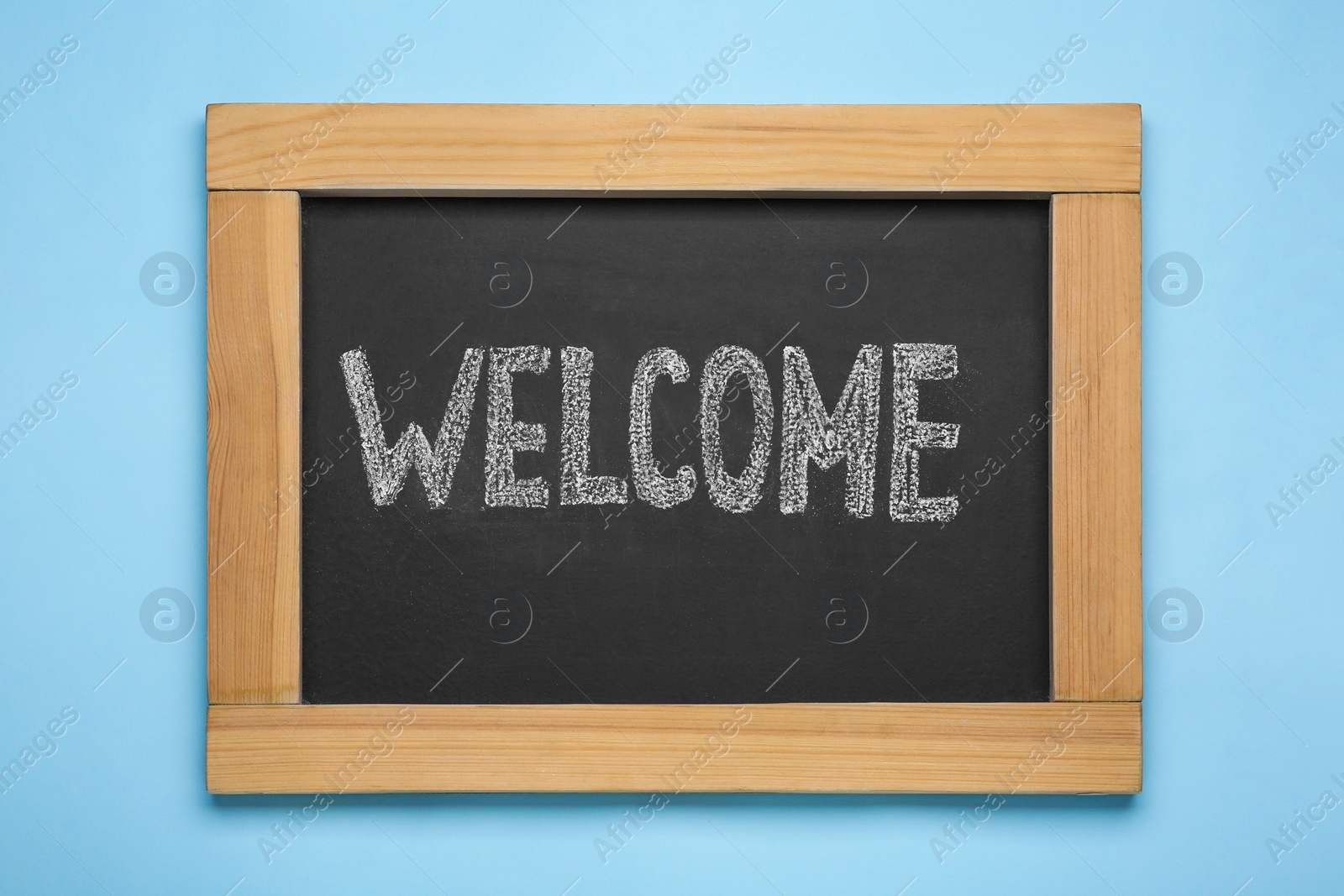 Photo of Small chalkboard with word Welcome on light blue background, top view