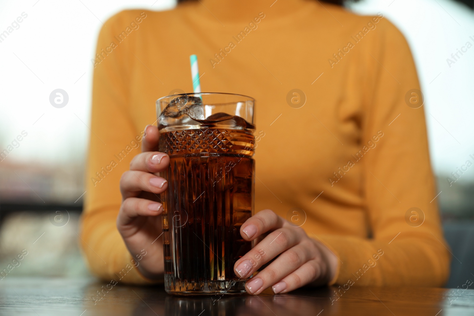 Photo of Woman with glass of refreshing cola at table indoors, closeup