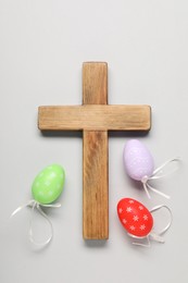 Wooden cross and painted Easter eggs on light grey background, flat lay