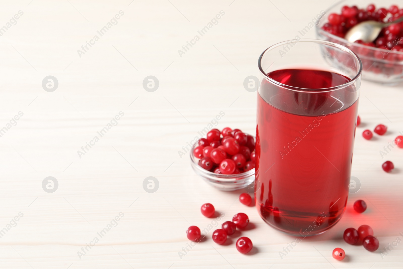 Photo of Tasty cranberry juice in glass and fresh berries on white wooden table, closeup. Space for text