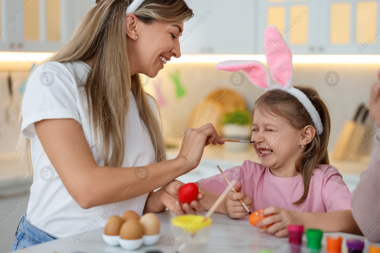 Photo of Easter celebration. Happy mother with daughter having fun while painting eggs at table in kitchen