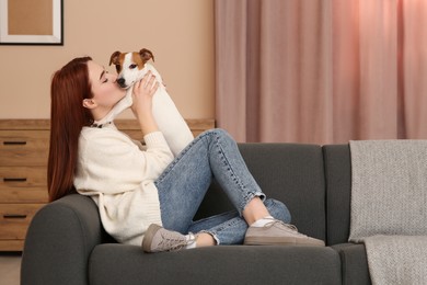 Photo of Woman kissing cute Jack Russell Terrier dog on sofa at home. Space for text