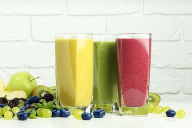 Photo of Fresh colorful fruit smoothies and ingredients on table against white brick wall