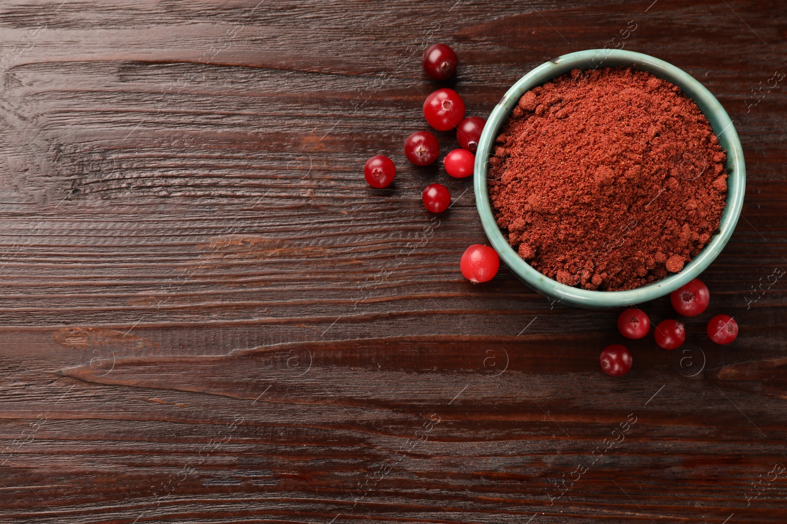 Photo of Dried cranberry powder in bowl and fresh berries on wooden table, top view. Space for text