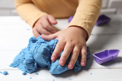 Photo of Little child playing with light blue kinetic sand at white wooden table, closeup