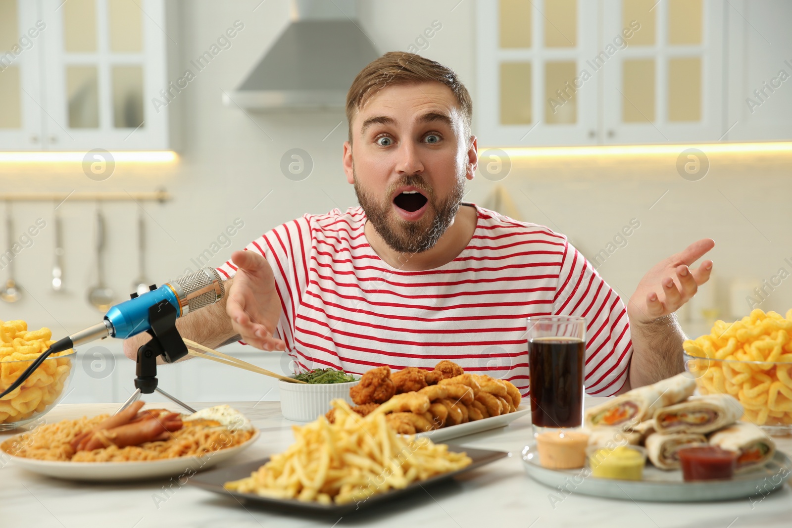 Photo of Emotional food blogger recording eating show near microphone at table in kitchen. Mukbang vlog