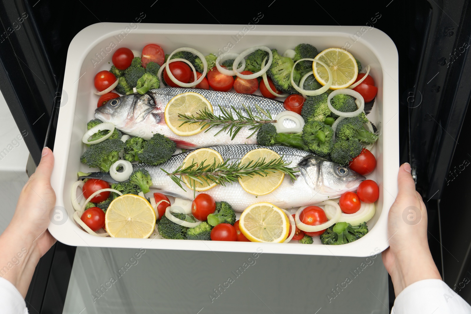 Photo of Woman putting baking dish with raw fish and vegetables into oven, top view