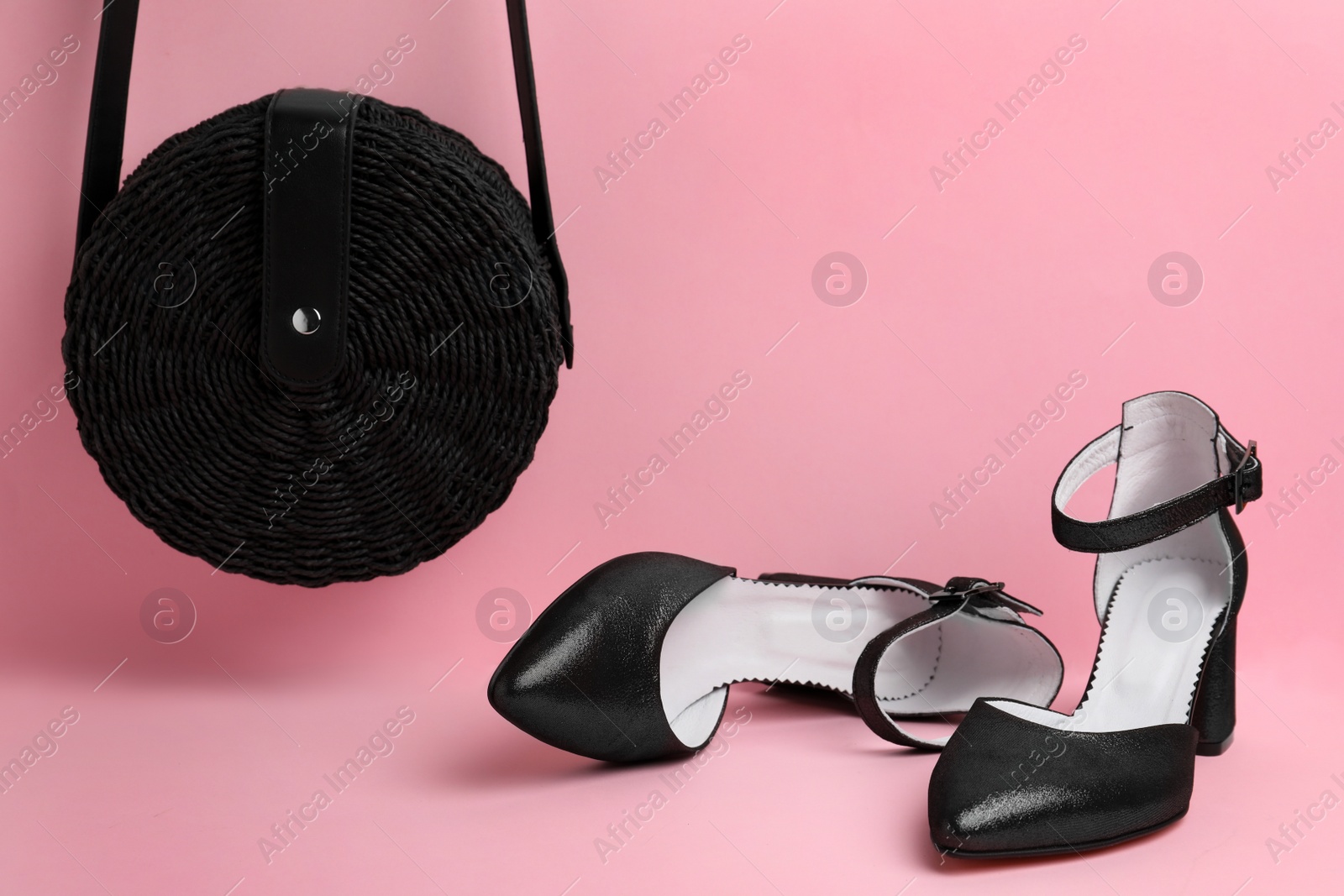 Photo of Stylish black female shoes and bag on pink background