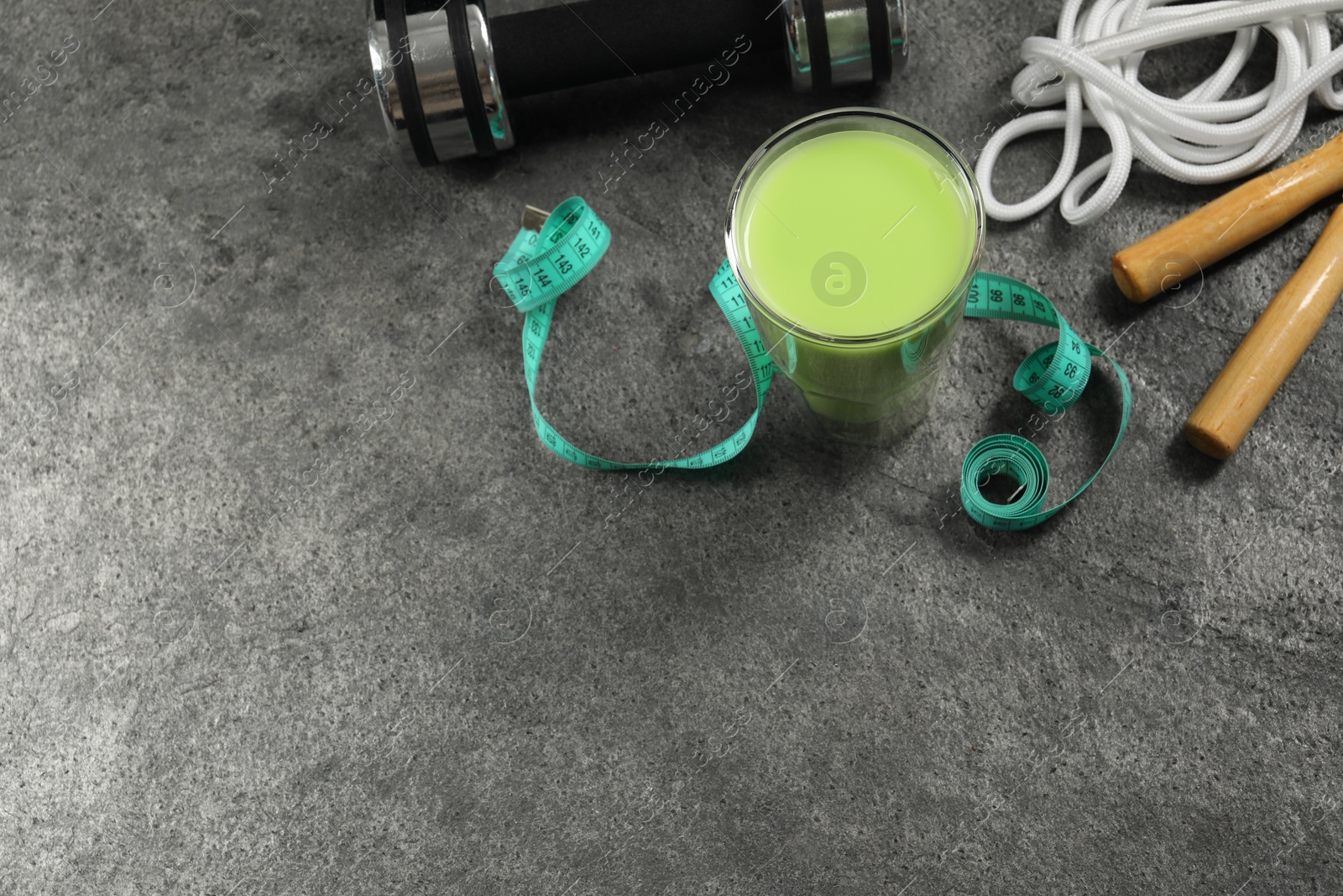 Photo of Tasty shake, sports equipment and measuring tape on stone table, above view with space for text. Weight loss