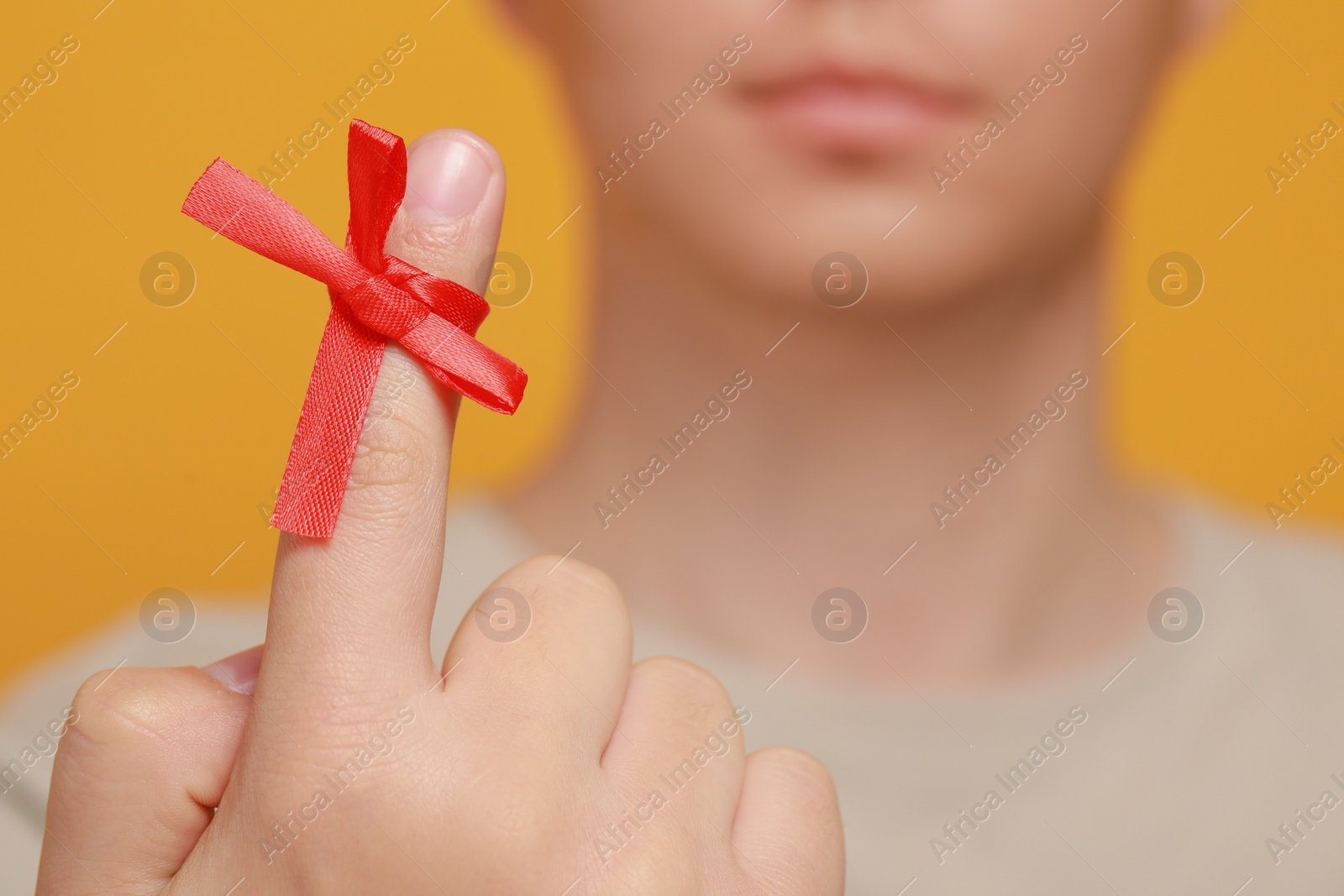 Photo of Man showing index finger with red tied bow as reminder against orange background, focus on hand