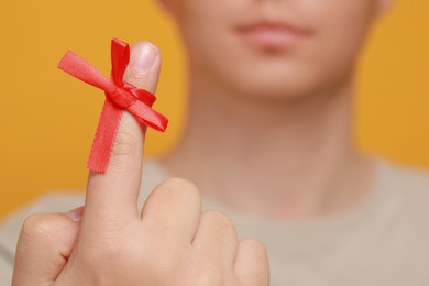 Photo of Man showing index finger with red tied bow as reminder against orange background, focus on hand