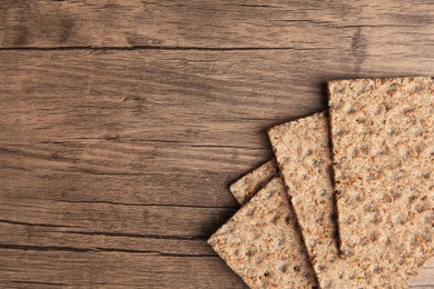 Photo of Fresh crunchy crispbreads on wooden table, flat lay. Space for text