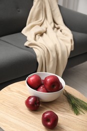 Red apples and coniferous branches on wooden coffee table near grey sofa indoors