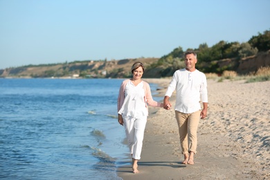 Happy mature couple walking at beach on sunny day