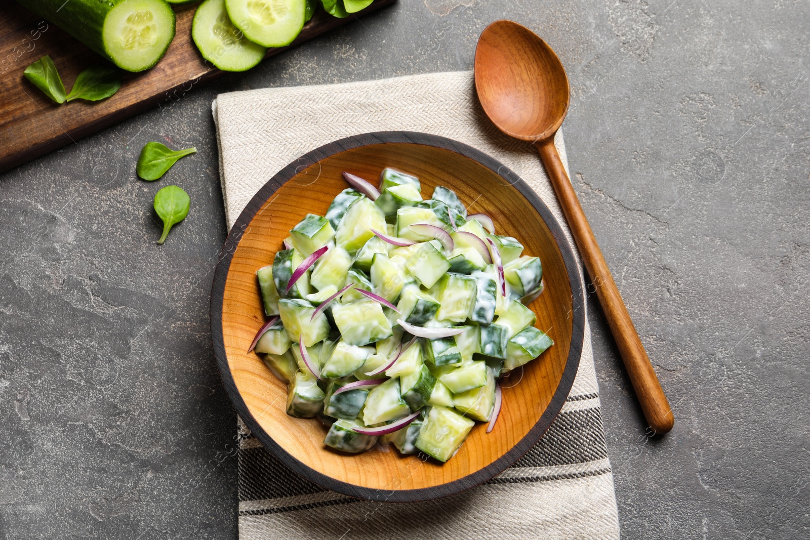 Photo of Flat lay composition with wooden plate of creamy cucumber salad on table