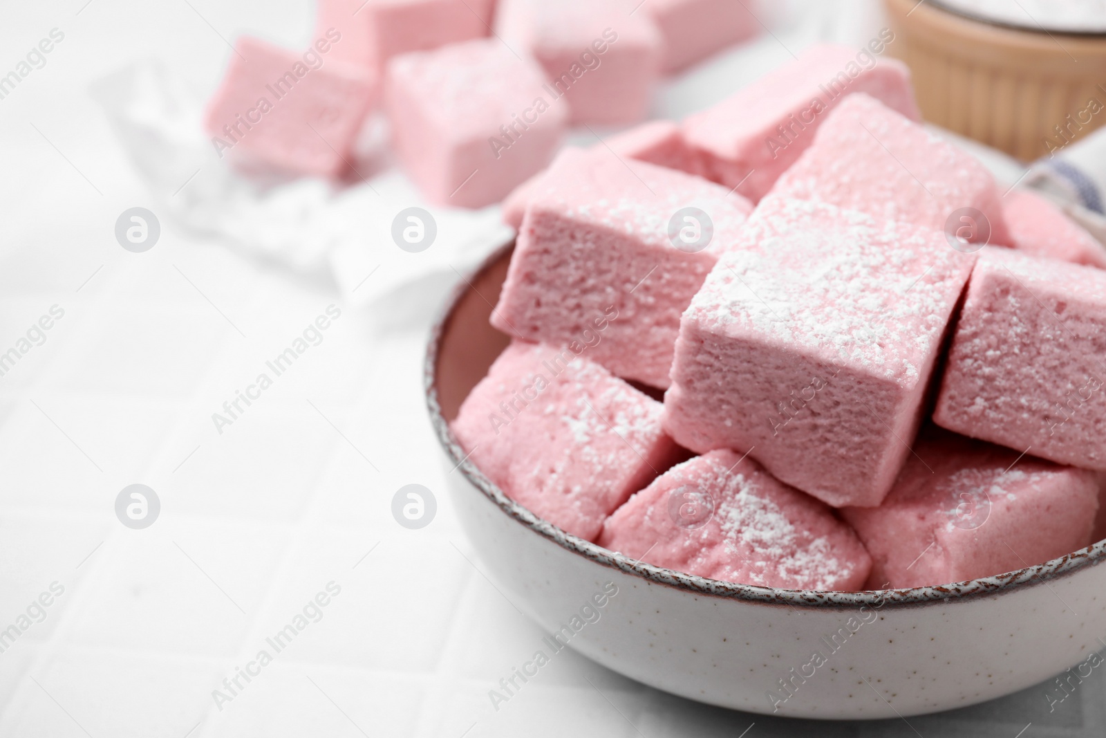 Photo of Bowl of delicious sweet marshmallows with powdered sugar on white table, closeup. Space for text