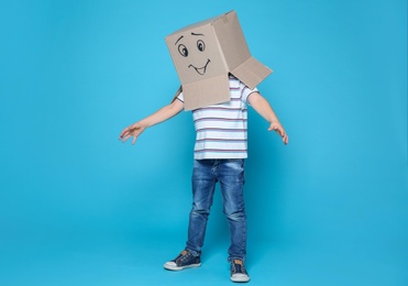 Cute little child wearing cardboard box with smiling face on color background