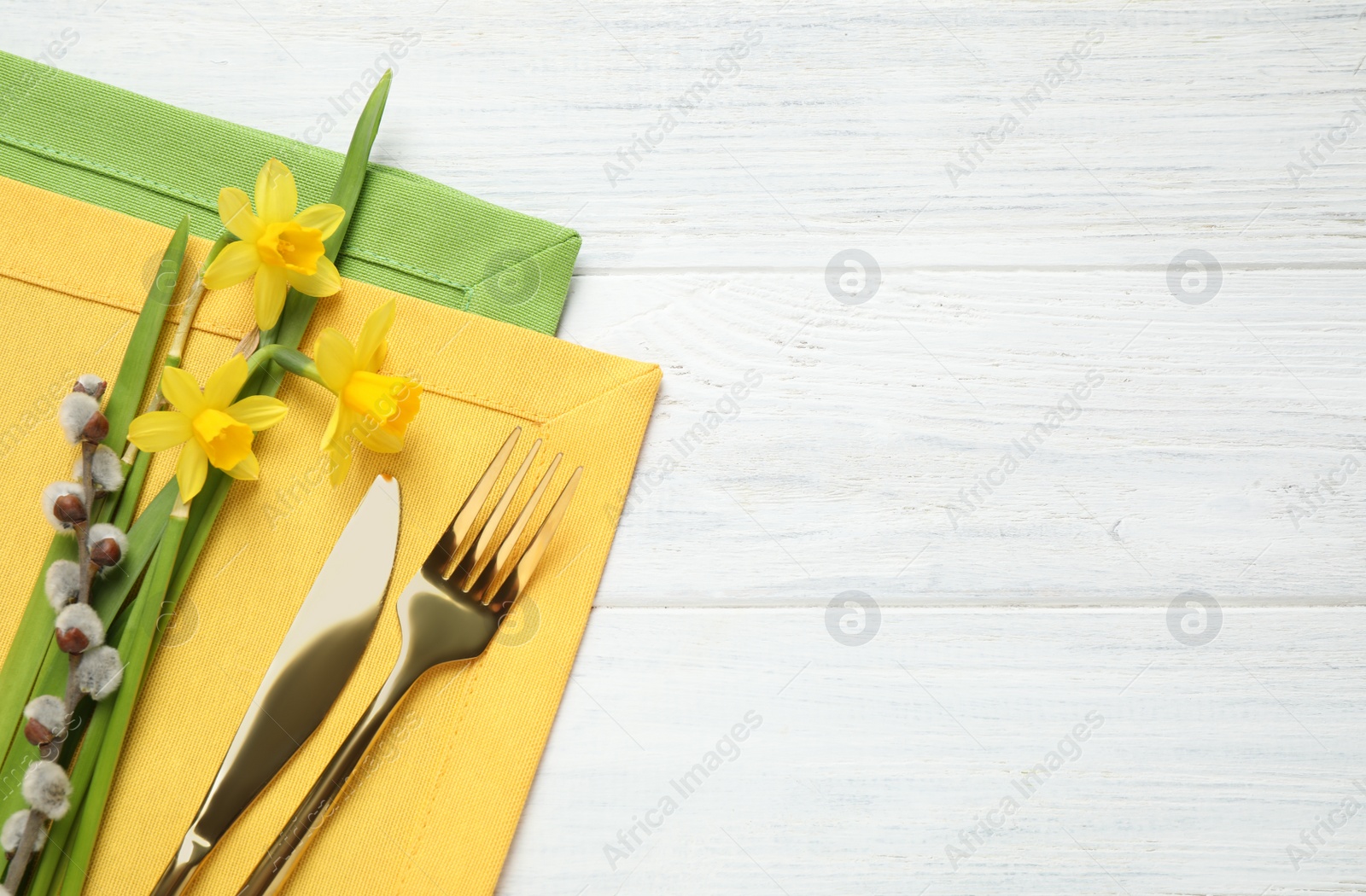 Photo of Cutlery set and floral decor on white wooden table, top view with space for text. Easter celebration