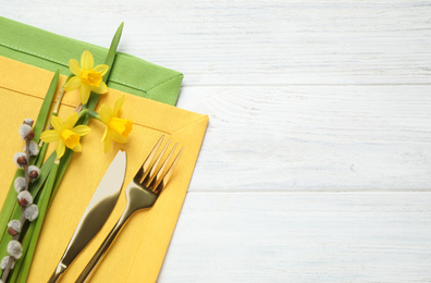 Cutlery set and floral decor on white wooden table, top view with space for text. Easter celebration