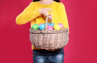 Little girl holding basket with Easter eggs on color background