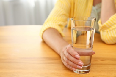 Photo of Woman holding glass of water at wooden table, closeup with space for text. Refreshing drink