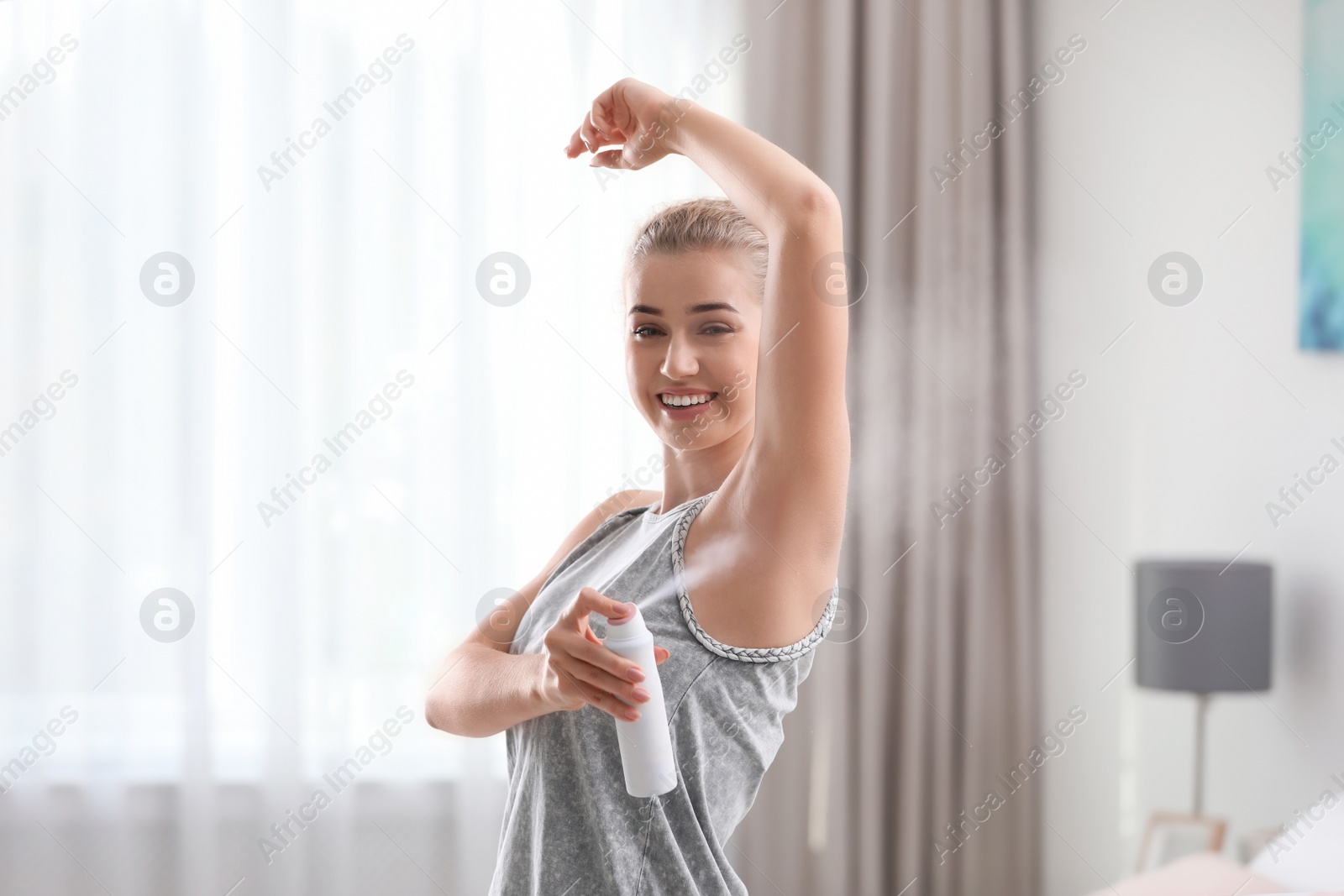 Photo of Beautiful young woman applying deodorant in bedroom