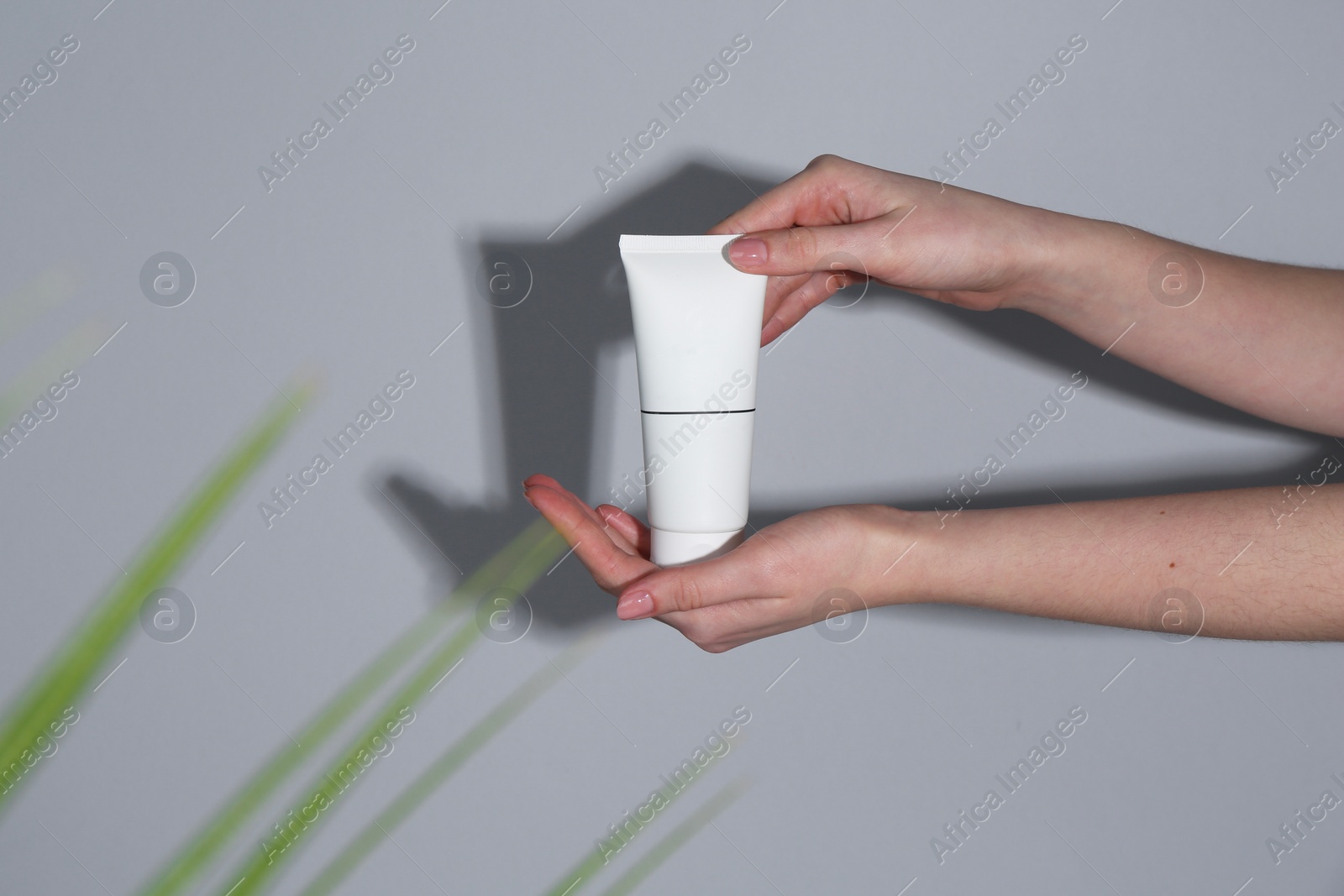 Photo of Woman holding tube of cream on grey background, closeup