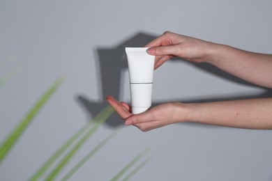 Woman holding tube of cream on grey background, closeup