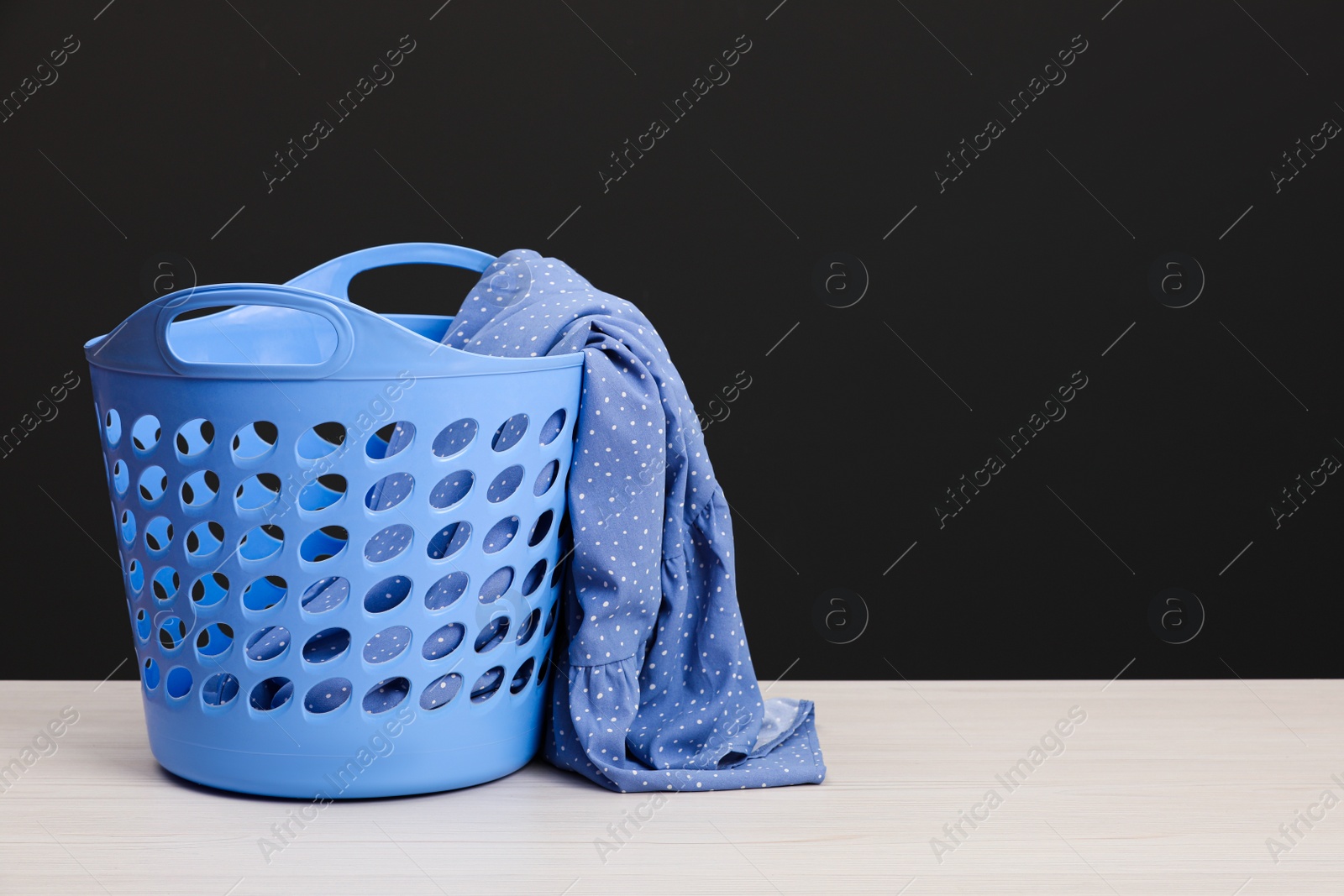 Photo of Plastic laundry basket with clothes near dark grey wall. Space for text