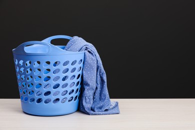 Photo of Plastic laundry basket with clothes near dark grey wall. Space for text