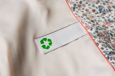 Clothing label with recycling symbol on light garment, closeup