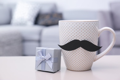 Cup with mustache and gift box on table. Father's day celebration