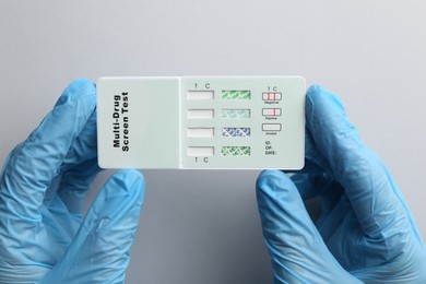 Photo of Doctor holding multi-drug screen test on light grey background, top view