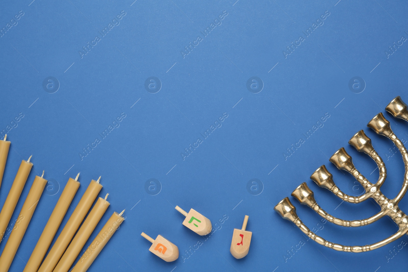 Photo of Golden menorah, yellow candles and Hanukkah dreidels with He, Pe, Gimel symbols on blue background, flat lay. Space for text