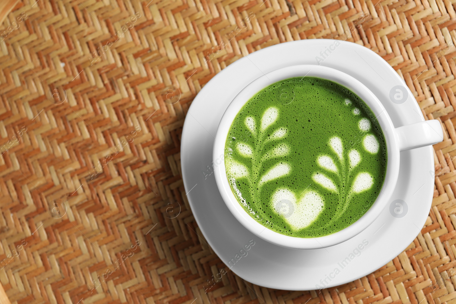 Photo of Delicious matcha latte in cup on wicker table, top view. Space for text